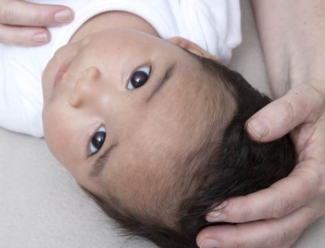 Hands gently supporting a baby’s head